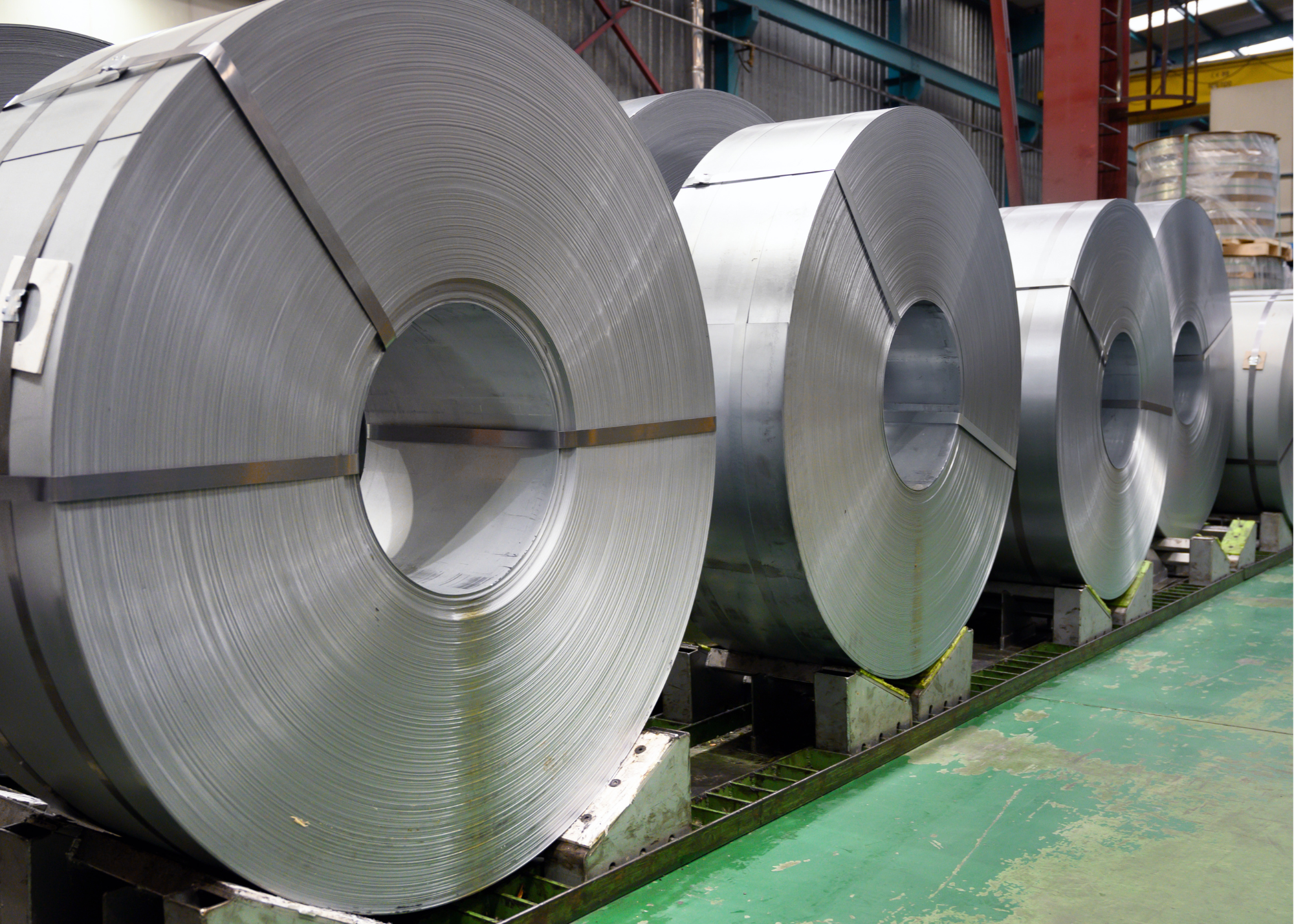Industrial coils of steel and copper next to stacked aluminum sheets in a manufacturing warehouse representing metal materials subject to Section 232 tariffs.
